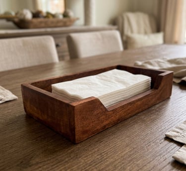 Handcrafted wooden napkin holder with white paper napkins on a rustic oak dining table.